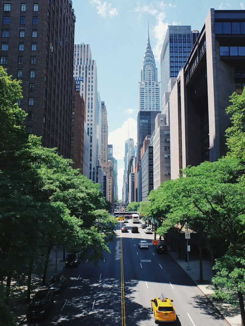 A Manhattan avenue running north between towers, a cab mid-block.